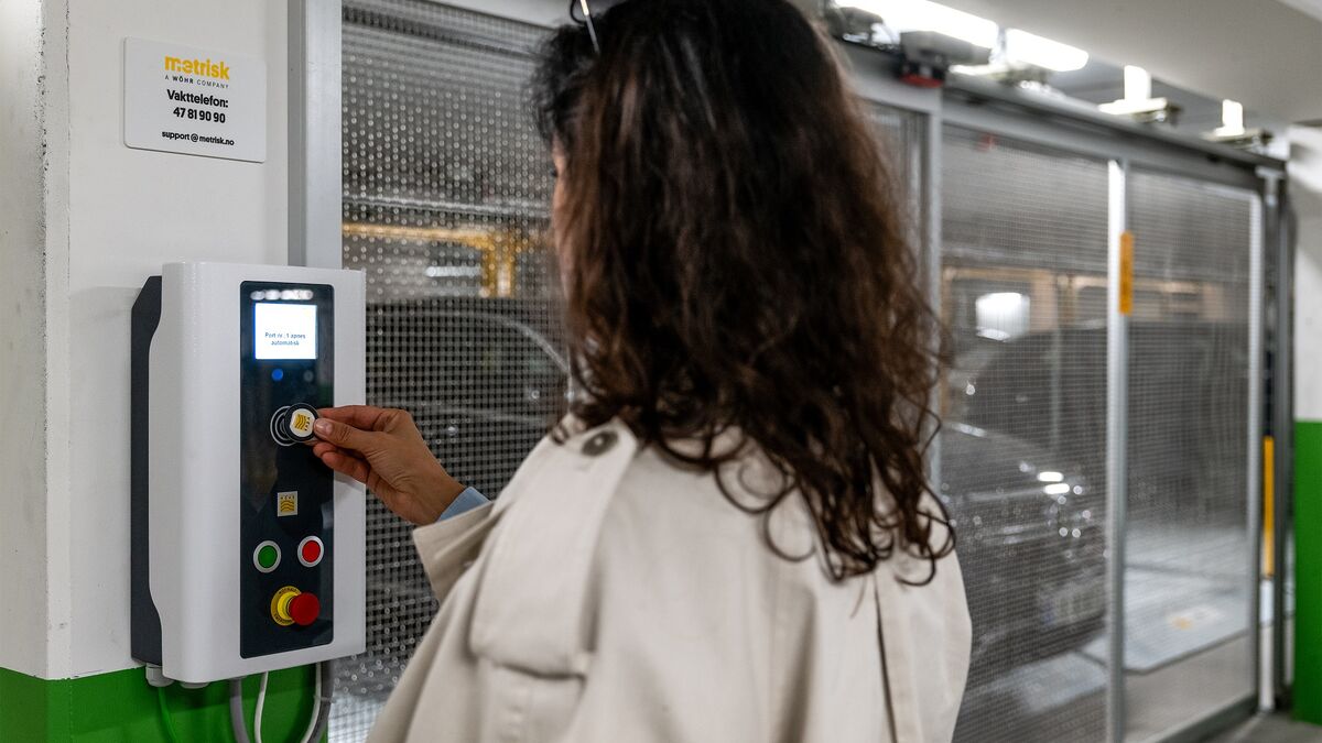 Eine Person bedient das Steuerungspanel eines halbautomatischen Parksystems, um das geparkte Fahrzeug abzurufen. Im Hintergrund sind die verschiebbaren Stellplätze und ein Fahrzeug innerhalb der Parkanlage sichtbar.