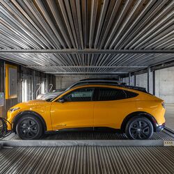 L'immagine mostra un'auto su una piattaforma all'interno di un sistema di parcheggio automatizzato in un moderno parcheggio sotterraneo.