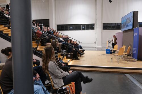 Pièce avec une personne à la tribune et d'autres personnes assises sur un escalier