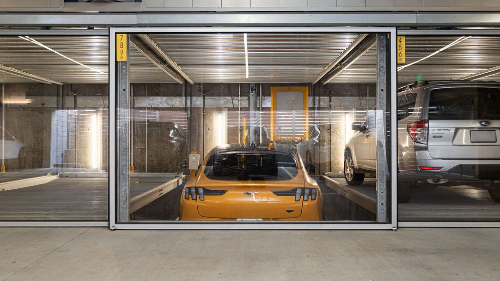 L'immagine mostra un'auto sportiva gialla in un sistema di parcheggio all'interno di un moderno parcheggio sotterraneo.