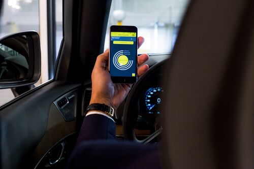 Frau sitzt im Auto und hält ein Handy mit geöffneter App vor sich