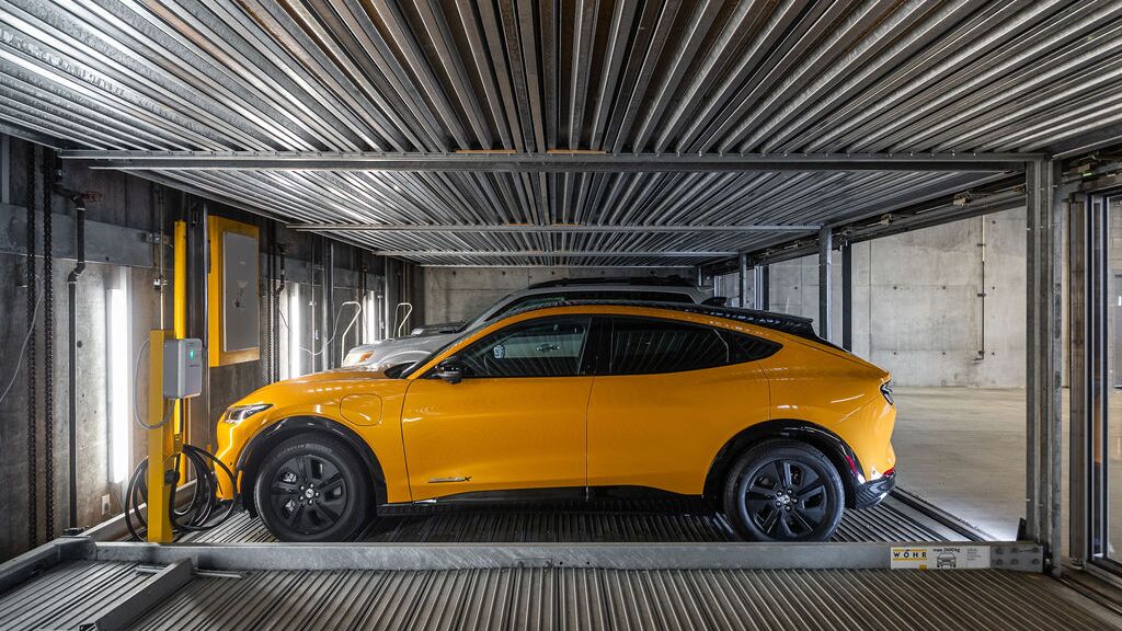 L'immagine mostra un'auto su una piattaforma all'interno di un sistema di parcheggio automatizzato in un moderno parcheggio sotterraneo.