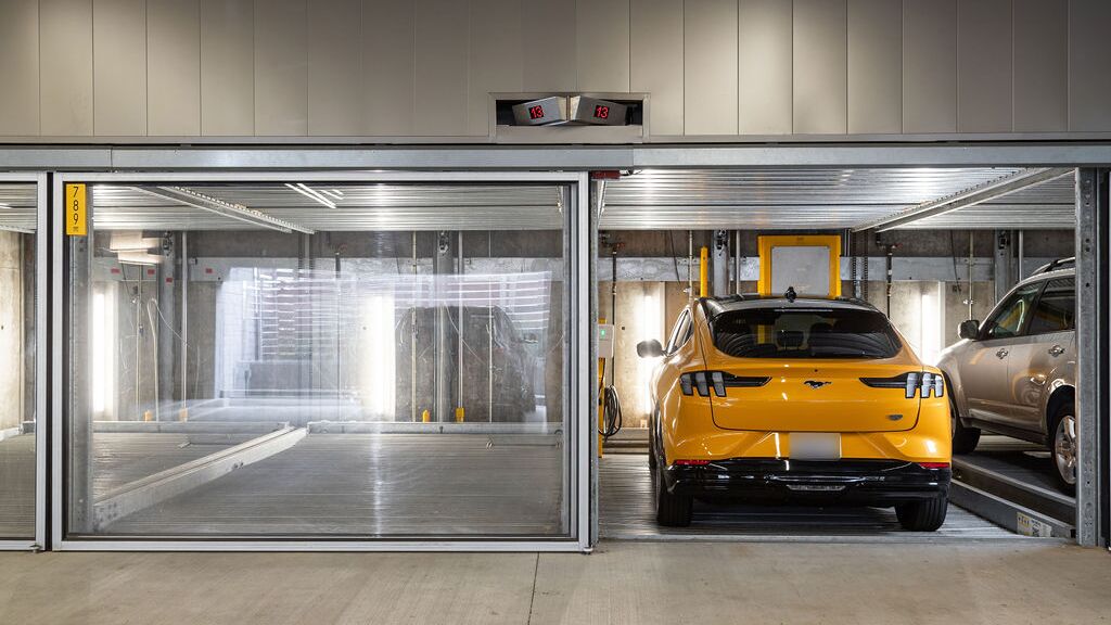 L'immagine mostra diversi veicoli in posti auto vetrati di un sistema di parcheggio in un moderno parcheggio sotterraneo.