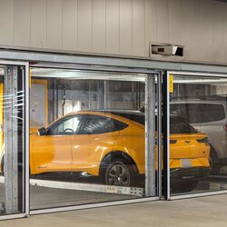 L'immagine mostra diversi veicoli in posti auto vetrati di un sistema di parcheggio in un moderno parcheggio sotterraneo.